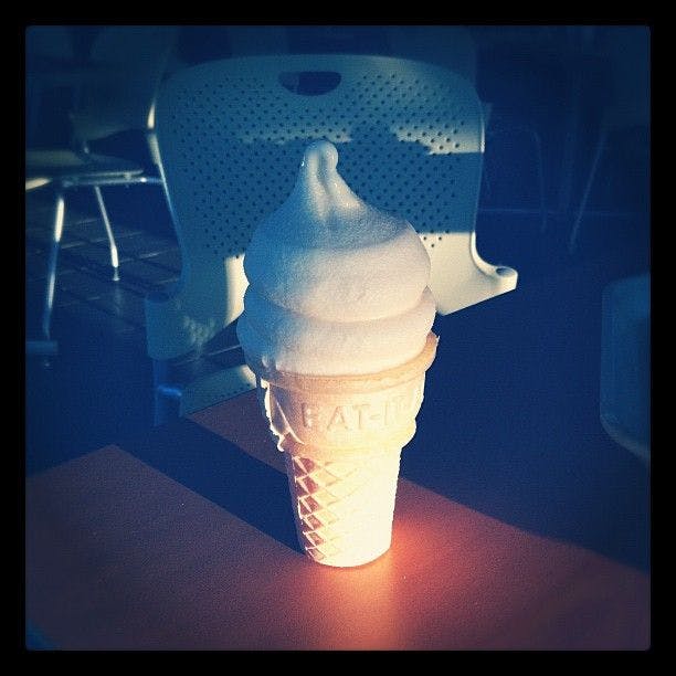 Photo of soft serve ice cream in a cone sitting on a table.